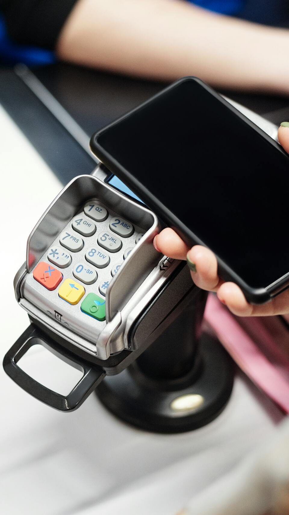 Close-up of a customer using a smartphone for contactless payment at a retail checkout with a pineapple on the counter.