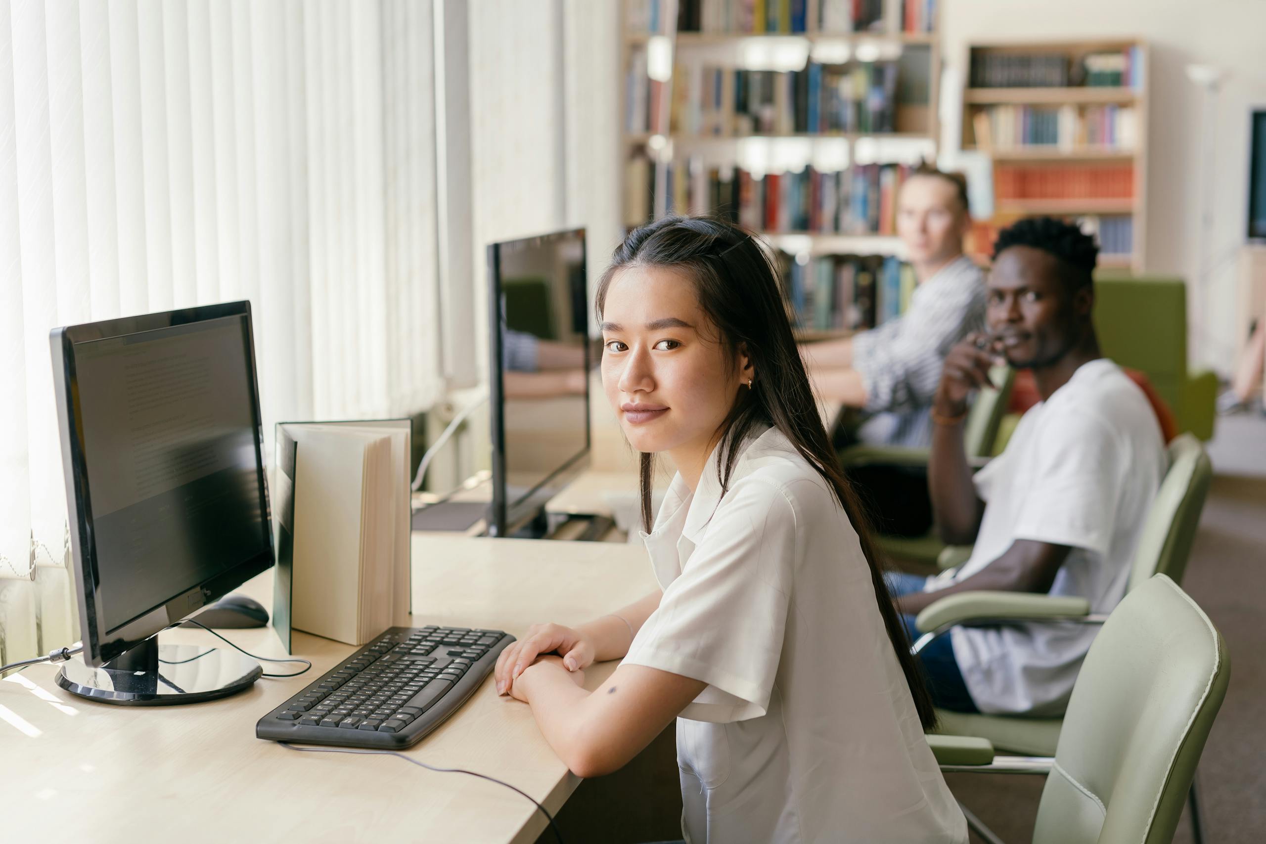 Students engaged in learning at a modern library with computers and natural lighting.